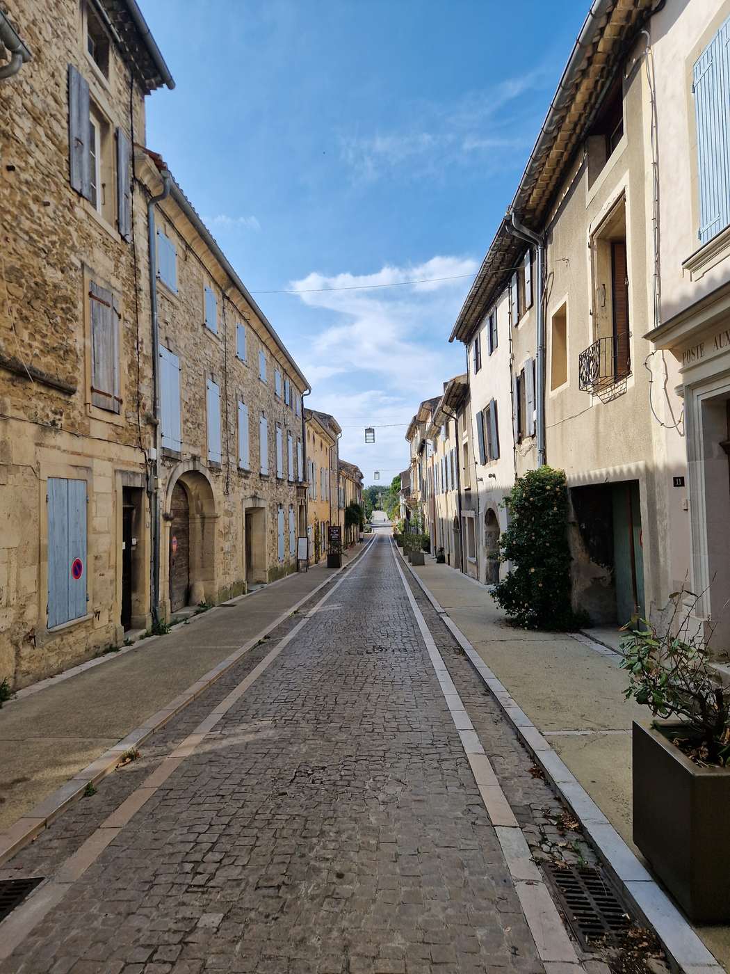 Une longue rue piétonne pavée de Grignan, bordée de maisons de pierre aux volets clairs